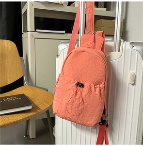 Detail of coral orange nylon sling bag with drawstring pocket hanging on a suitcase