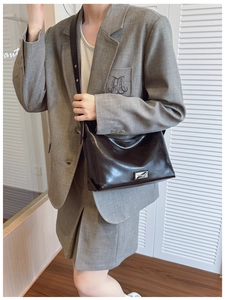 Glossy black shoulder bag with metal plate detail shown in a stylish urban outfit setting