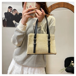 Detail shot of woven straw crossbody bag with black leather strap and silver buckle