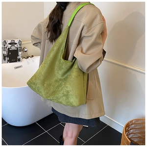 Detailed side view of green suede tote bag worn by a model in a minimalist setting