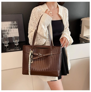 Detail of dark brown woven tote bag with smooth leather trim and white decorative charm