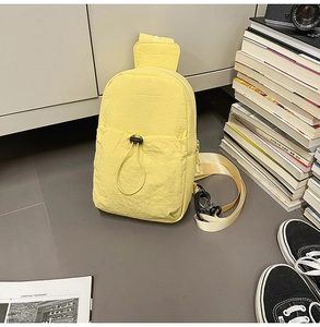 Detail of light yellow nylon chest bag featuring textured fabric and black drawstring toggle