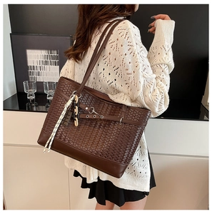 Detail of dark brown woven leather tote bag with stylish decorative charms and strap