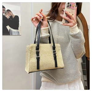 Detail of hand-woven straw tote with black leather straps and metal buckle accents