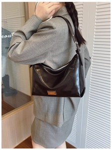 Detail of dark brown leather shoulder bag with metallic logo and adjustable strap