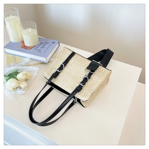 Detail of a rectangular straw woven tote bag with black leather straps and silver buckles