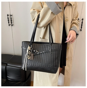Detail of black woven tote bag featuring intricate texture and decorative strap charm
