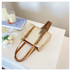 Detail of woven straw tote bag featuring brown leather straps and silver hardware accents