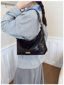 Detail of black leather underarm bag featuring silver zipper and rectangular metal logo