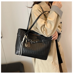 Close-up of black woven texture tote bag featuring metallic eyelets and decorative charms
