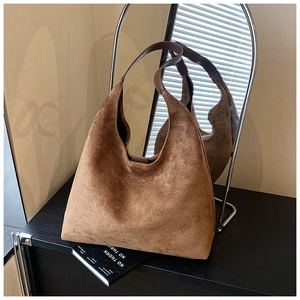 Detail of mocha brown suede tote bag with leather strap on minimalist dark shelf