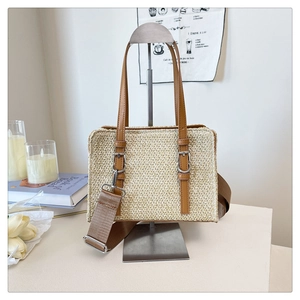 Detail of woven straw tote bag with brown leather straps and adjustable fabric shoulder strap