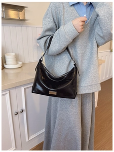Detail of glossy black leather shoulder bag with metallic zipper and rectangular hardware