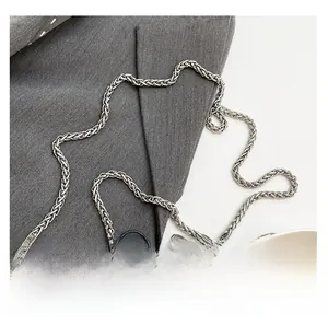 Close-up of a silver woven metal chain strap for handbags on gray blazer fabric