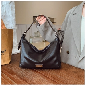 Detailed view of silver brand logo plate and polished leather texture on brown hobo bag