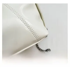 Close-up of white glossy patent leather handbag with silver chain and stitched corner