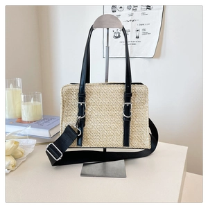 Close-up of woven straw tote bag with black leather handles and silver hardware detailing