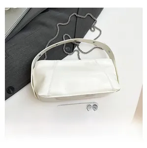 Detail view of white glossy handbag with silver rivets and metal chain on a grey blazer