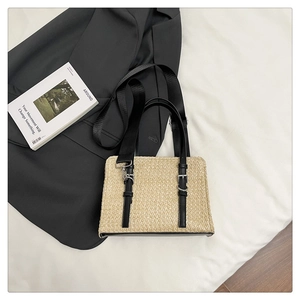 Detail of woven straw tote bag with black straps and adjustable metal buckles