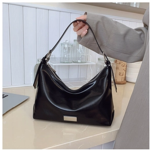 Detail of glossy black leather hobo bag with silver logo plate and integrated strap