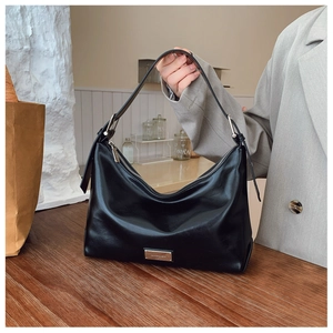 Detailed view of black polished leather hobo bag with gold metal logo on wooden table