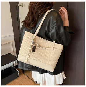 Detail of a beige woven tote bag with V-pattern texture and chocolate charm on a model
