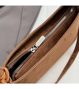 Detailed close-up of smooth silver metal zipper on coffee brown suede shoulder bag