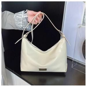 Close-up of adjustable shoulder strap and silver metal logo on beige glossy shoulder bag