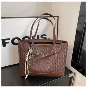 Detail of a brown woven tote bag with a unique chocolate pendant on a minimalist stand