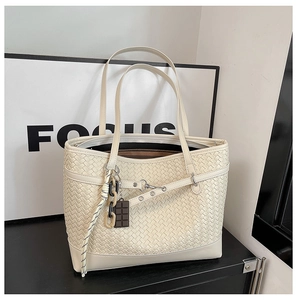 Close-up of woven cream tote bag with leather buckle details and stylish chain charm