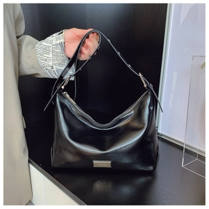 Detail of silver brand plaque on a black glossy minimalist underarm bag with zipper