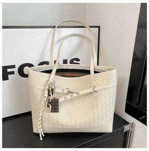 Detail of woven beige tote bag with a chocolate-shaped charm and braided cord accent