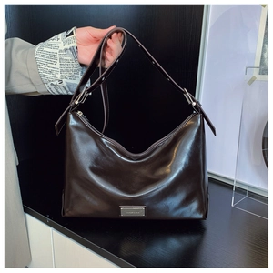 Close-up of dark brown glossy leather hobo bag with metal logo and adjustable strap