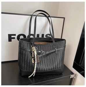Detailed close-up of black woven tote bag with silver metal buckles and decorative charms