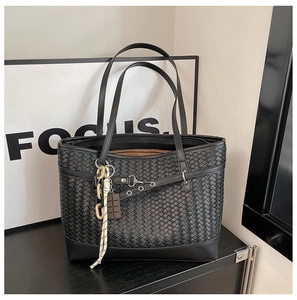 Detailed close-up of a black woven tote bag featuring a leather strap with metal eyelets