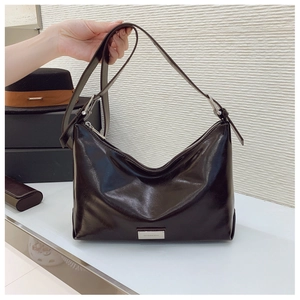 Close-up of polished dark brown leather shoulder bag with metallic logo plaque