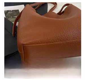 Detail showing precise stitching and litchi grain texture on the brown leather bucket bag