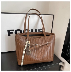 Detailed macro view of deep brown woven leather texture and elegant ribbon charm on tote bag