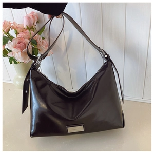 Detail of black glossy leather crescent shoulder bag with silver brand plaque and wide strap