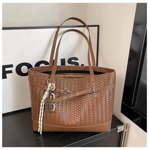Detailed close-up of brown woven texture tote bag with stylish chocolate charm and tassel