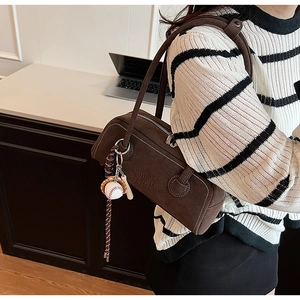 Macro detail of brown suede Boston bag with baseball pendant and embossed logo texture