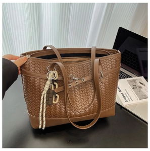 Close-up of brown woven tote bag with creative charm and belt buckle detail on desk