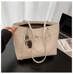 Detail of cream woven tote bag with metallic zipper and stylish decorative charms on a desk
