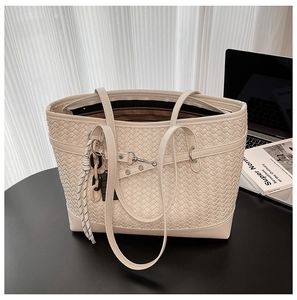 Detail of the woven texture and chain ornament on a cream oversized leather tote bag
