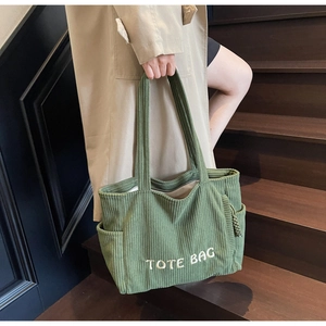 Détail d'un sac cabas en velours côtelé vert avec broderie blanche sur escalier