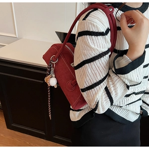 Detail of burgundy matte suede boston bag with baseball glove pendant and shoulder strap