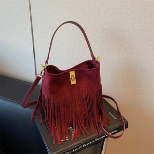Detail of burgundy fringe bucket bag showing suede texture and gold square turn-lock closure
