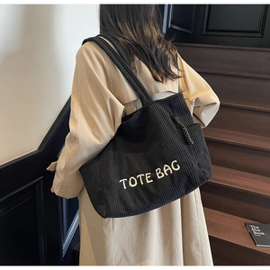 Détail d'un cabas en velours côtelé noir avec broderie TOTE BAG sur un mannequin