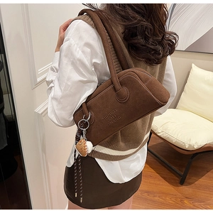 Close-up of brown suede Boston bag with embossed lettering and baseball keychain