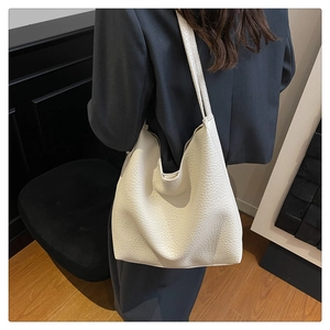 Close-up of a white lychee grain leather bucket bag worn by a model in a gray suit